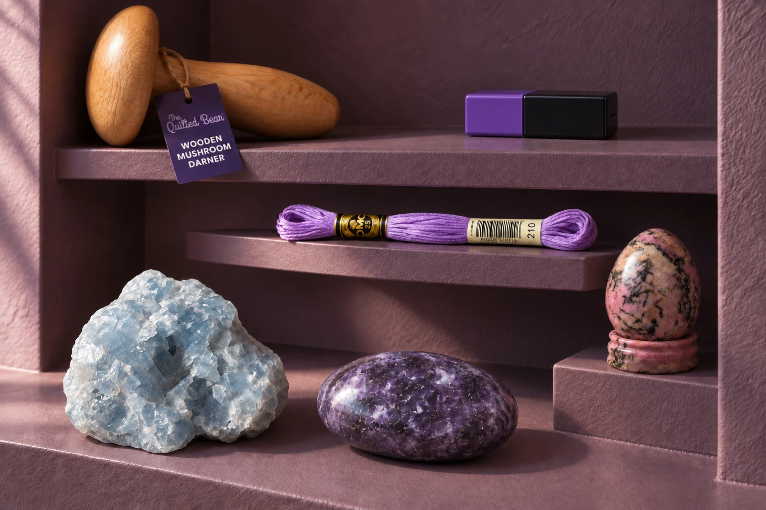 A rough blue calcite, lilac lepidolite palm and rhodonite egg on a small stand sit in a dark plum mending alcove with a beech darning mushroom, lilac floss skein and purple-and-black magnetic needle case.